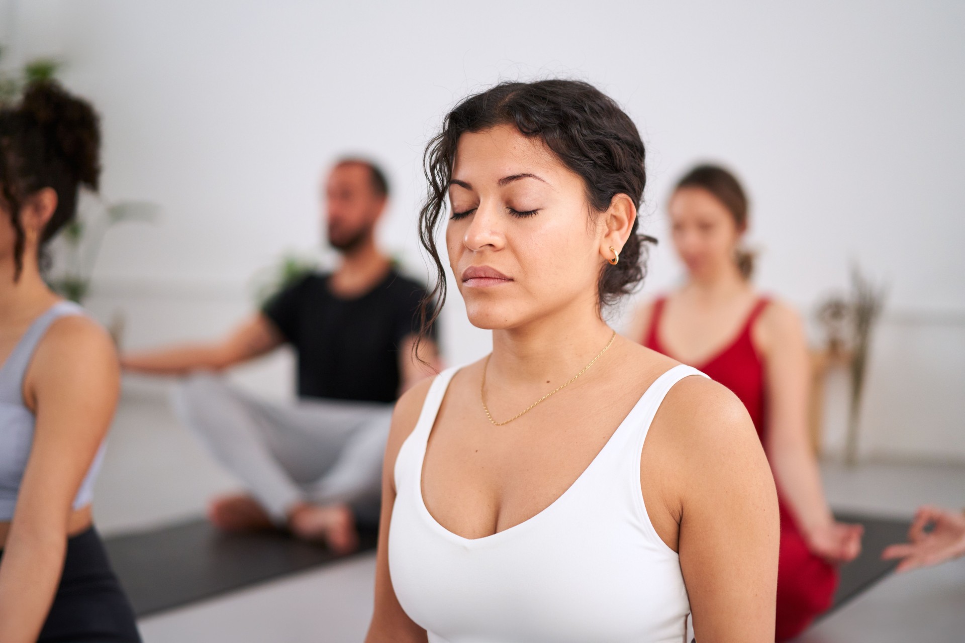 Close-up young Latina woman with eyes closed practising yoga exercises indoors. Group of people